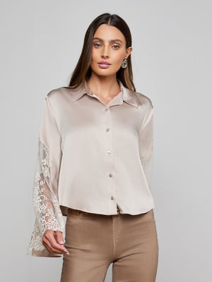 A woman wears the Capri Lace Sleeve Blouse with relaxed fit and lace bell sleeves, paired with light brown pants, standing against a plain light gray background.