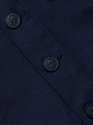 Close-up of the Anouk Jean Jacket in navy blue stretch denim, featuring a diagonal seam and four dark decorative buttons. The collarless design highlights the jacket’s tight weave and texture.