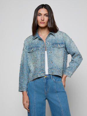 A woman with straight brown hair models the Vangie Embellished Jean Jacket over a white top and blue jeans, standing against a plain light gray background.