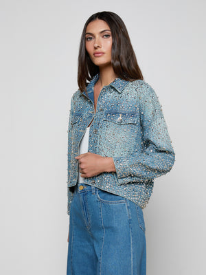 A woman with long brown hair models the Vangie Embellished Jean Jacket, adorned with crystals and silver studs, paired with blue jeans against a plain light background.