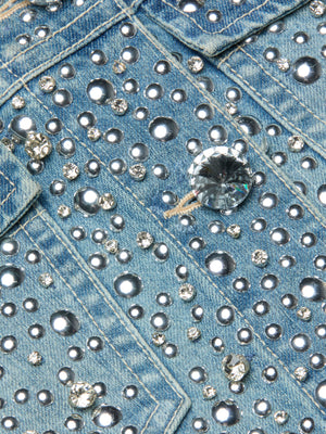 Close-up of the Vangie Embellished Jean Jacket, featuring blue denim decorated with round and faceted silver and clear rhinestones that create a sparkling, textured look. Visible pocket seams and stitching add extra detail to this standout piece.
