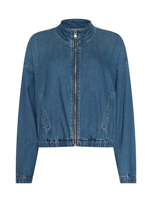 The Dunia Jean Jacket is a blue cotton denim jacket with a relaxed fit, front zipper, long sleeves, two slanted front pockets, elastic cuffs and hem, and a lightweight collarless design.