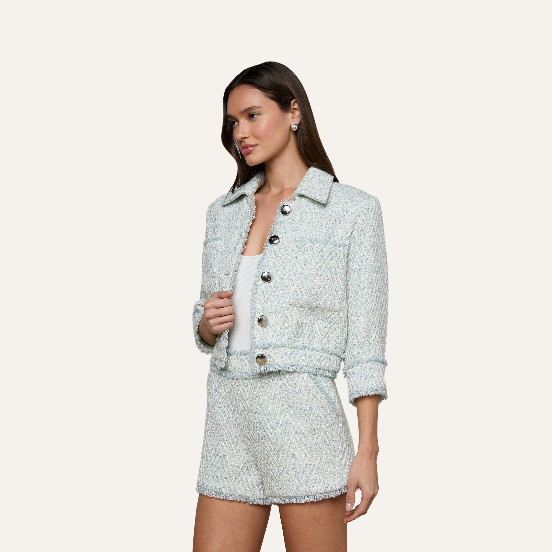 A woman wearing the Jia Fringed Tweed Jacket in light blue with large buttons and matching high-waisted shorts, standing against a plain white background.
