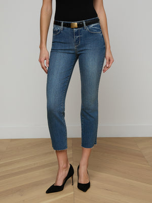 Wearing Sada Cropped Slim-Leg Jean in blue stretch denim, a black top, black belt, and black high-heeled shoes, a person stands on a wooden floor against a plain light-colored wall.