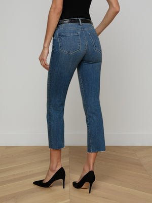 Wearing the Sada Cropped Slim-Leg Jean in stretch denim and black high heels, a person stands on a light wooden floor facing away from the camera against a plain white wall.