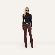A person wearing a black turtleneck, a black belt with a large gold buckle, and Ruth Coated Straight-Leg Jean high-rise, straight-leg coated stretch denim jeans.