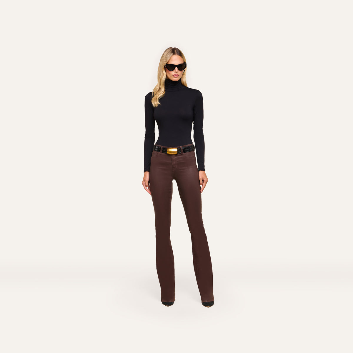 A person wearing a black turtleneck, a black belt with a large gold buckle, and Ruth Coated Straight-Leg Jean high-rise, straight-leg coated stretch denim jeans.