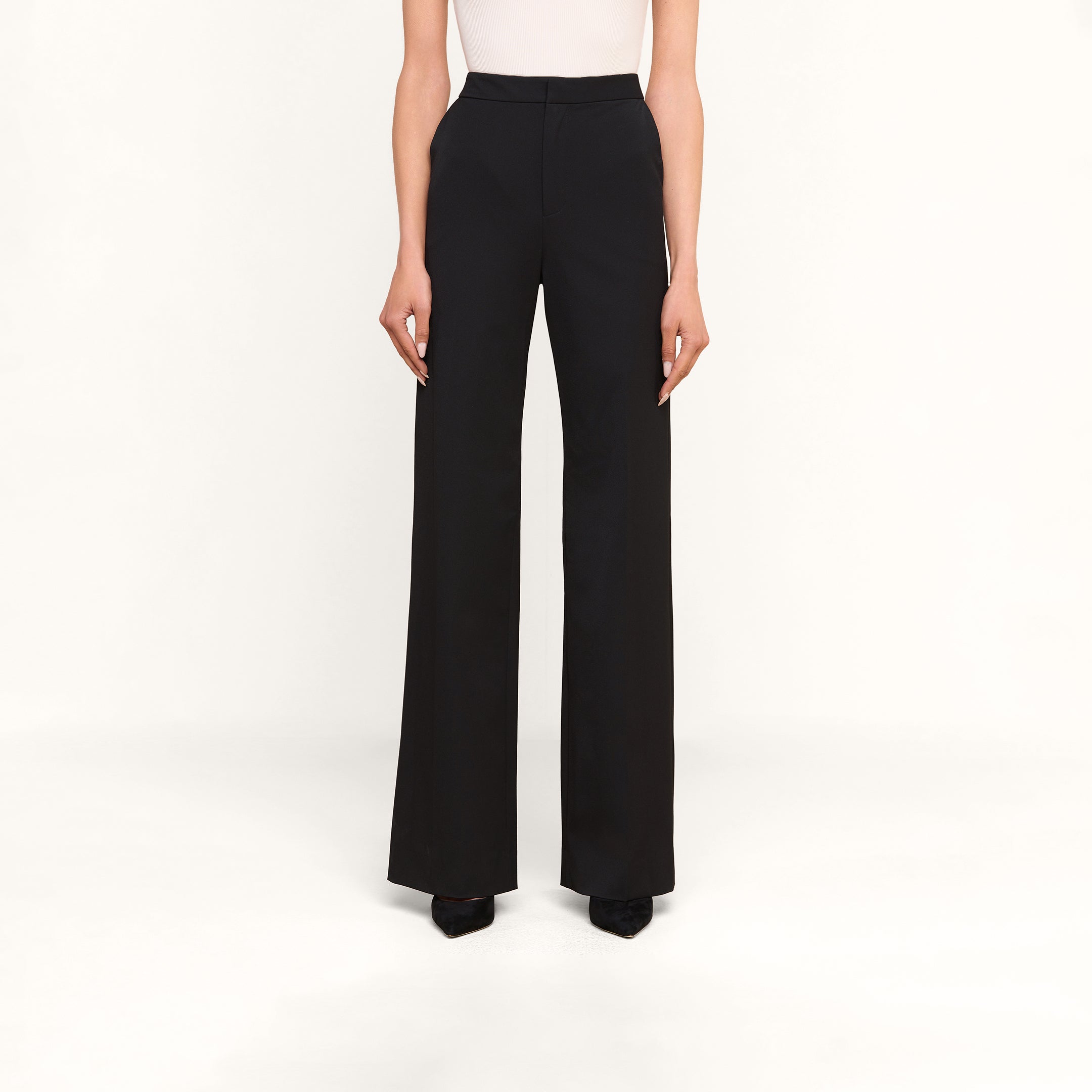 Porté avec le pantalon Livvy noir, à taille haute et coupe large, associé à des chaussures noires classiques, ce look se détache sur un fond beige uni, pour un chic naturel, du bureau au dîner.