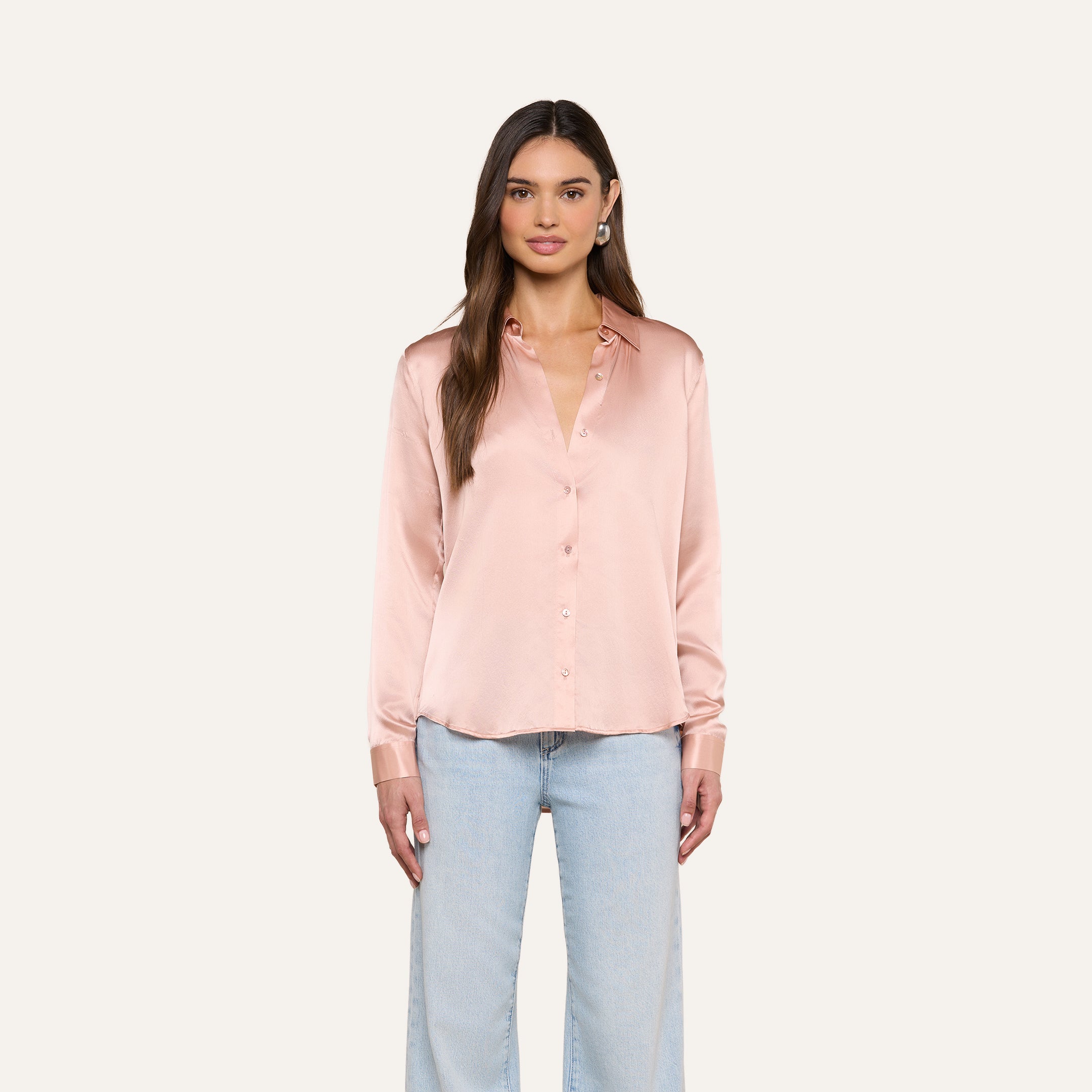 A woman wearing the Tyler Silk Blouse in pale pink and light blue jeans stands facing forward against a plain light background.