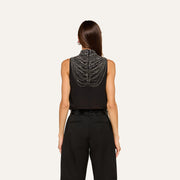 A person with straight brown hair wears the Yun Draped Crystal Tank—a sleeveless black blouse adorned with intricate beaded chains draping across the back—styled as an elegant evening top and paired with high-waisted black pants, shown from behind against a plain light background.