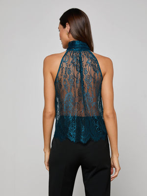 A woman with long brown hair models the Reece Lace Tie Neck Blouse, a sleeveless teal floral halter top, paired with black pants and shown from the back against a plain light gray background.