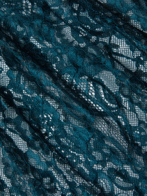 The Reece Lace Tie Neck Blouse features dark teal floral Chantilly lace with sheer sections and delicate, overlapping threads. Its slightly wrinkled texture adds depth, making it perfect for a stylish sheer lace blouse design.