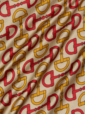 A close-up of the Calista Silk Camisole by L’AGENCE shows beige silk with interlocking gold and red horse bit print, resembling equestrian tack. The slightly wrinkled fabric is ideal for a chic cropped top or camisole.
