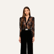 A woman wearing the Dorothea Velvet Lace Blouse with long sleeves, paired with high-waisted black pants, stands against a plain light background.