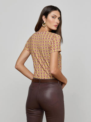A woman with long brown hair wears gold hoop earrings, high-waisted brown pants, and the Ressi Fitted Tee—a stretch jersey knit short sleeve top featuring a red and yellow graphic horse bit print—while looking over her shoulder.