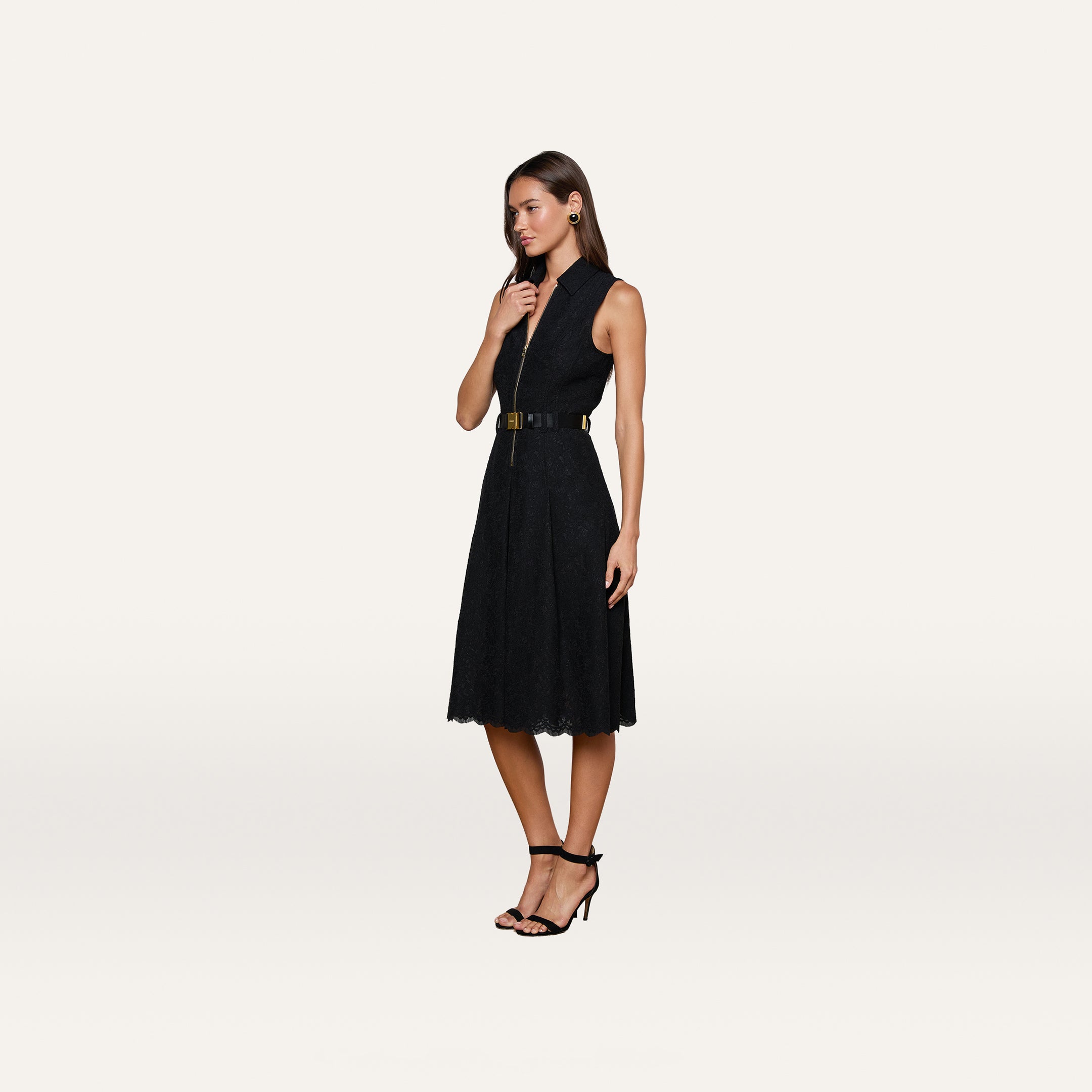 A woman wears the Kylo Lace Shirt Dress, a sleeveless black floral lace design paired with a wide belt and black high-heeled sandals, standing against a plain white background.