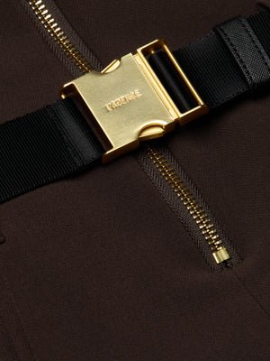 Close-up of the Kylo Shirt Dress by L’AGENCE: a black fabric strap with a shiny gold buckle fastened over dark brown suit fabric, featuring a prominent gold zipper running vertically beneath the strap.