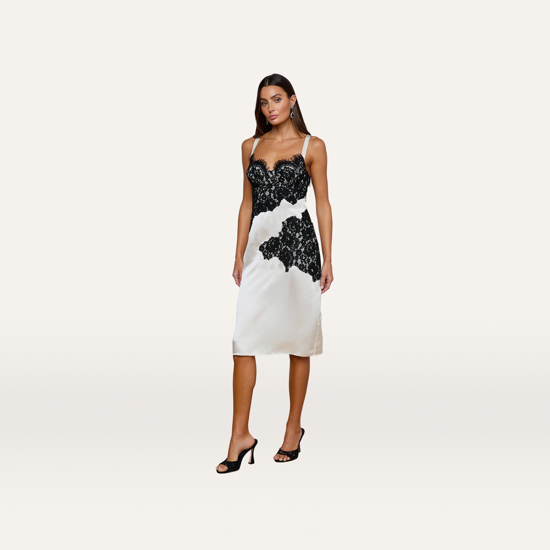 A woman poses confidently against a plain white background in the Fenna Silk Lace Dress, styled with black heeled sandals.