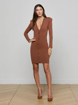 A woman poses against a light-gray background wearing the L'AGENCE Taru Button-Front Mini Dress, featuring a sculpted fit, long sleeves, deep V-neckline, and gold buttons. She pairs the brown mini dress with matching brown high heels.