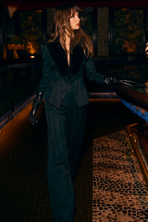 Woman in a dark green outfit standing in a dimly lit room with patterned carpet.