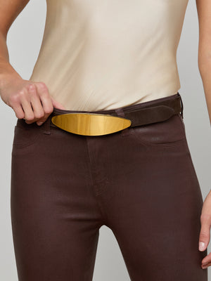 A person wearing high-waisted brown pants and a beige satin top holds the waistband to showcase the Maroux Leather Belt—a coffee brown, LA-handcrafted belt with a wide gold-plated buckle.