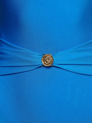 A close-up of the Lisa Plunge One-Piece Swimsuit in bright blue, showcasing moderate coverage and a gathered center accentuated by a round, gold decorative button with an intricate design.