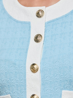 Close-up of the Adaline Cardigan Cover-Up in powder blue textured fabric, featuring white trim and four gold buttons with an embossed lion crest down the front.