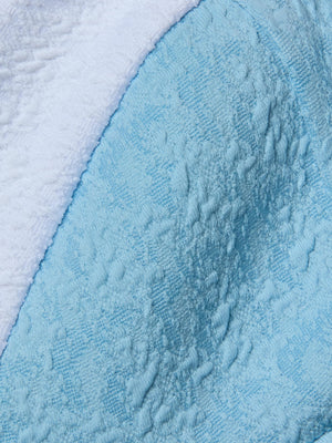 Close-up of bouclé swim fabric with a curved border; the top is white and the bottom is powder blue, both with a soft, towel-like look—ideal for the modern Alexandria Bikini Top.