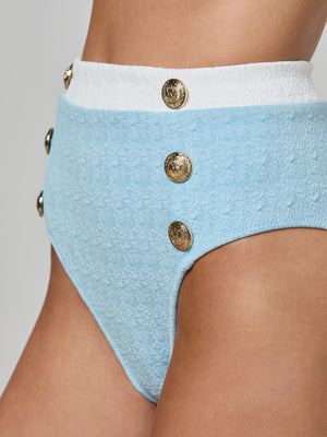 Close-up of a person wearing the Vanessa High-Waisted Bikini Bottom in textured light blue bouclé swim fabric, featuring a white waistband and gold decorative buttons, offering support and moderate coverage.