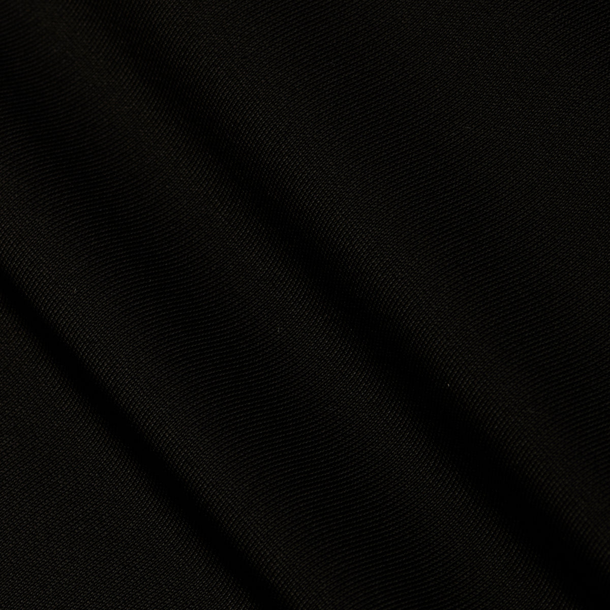 A close-up of black fabric from the Gabrielle One-Piece Swimsuit, featuring subtle diagonal folds and a fine, textured weave that evokes minimalist elegance.