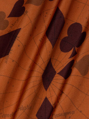 Close-up of the Akiya Satin Maxi Dress by L'AGENCE in burnt orange bias-cut satin, featuring dark playing card suit prints and subtle geometric lines—perfect for a standout look with natural folds and elegant texture.