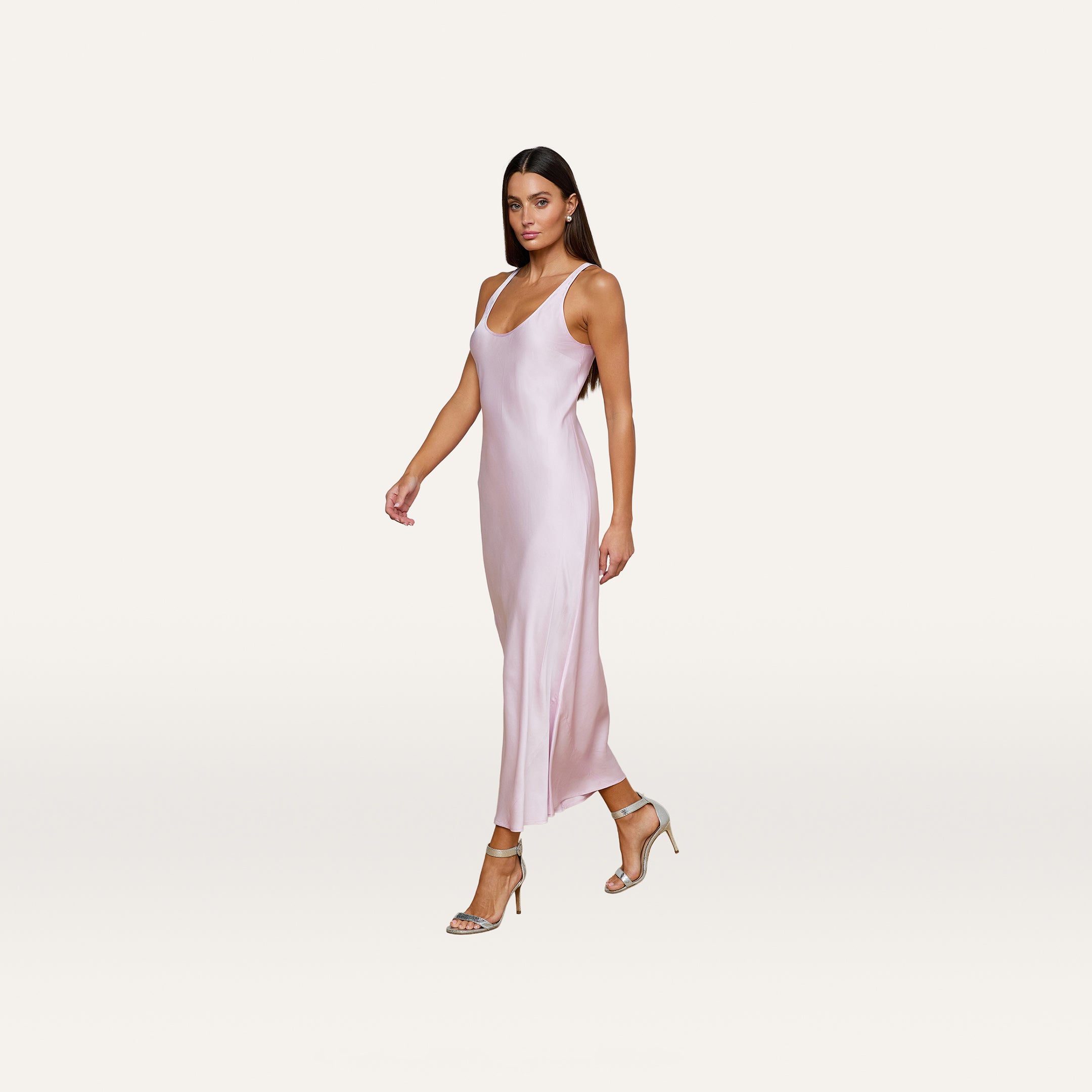 Wearing the Akiya Satin Maxi Dress in a sleeveless, pastel lilac design, a woman in strappy heels walks confidently against a plain, light background.