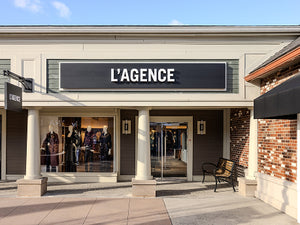 Storefront of L'AGENCE with mannequins inside, clear glass doors, and a bench outside.