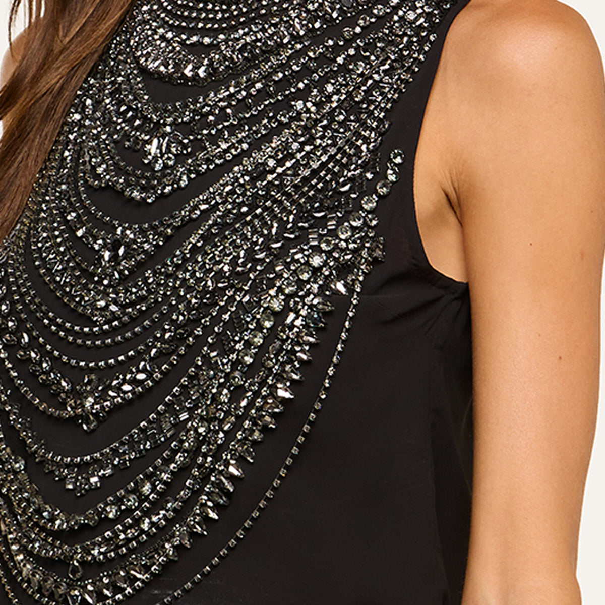 A close-up of a sleeveless black top showcases elaborate silver and black beaded embellishments, creating layered, draped patterns across the front and shoulders for a striking, sophisticated look.